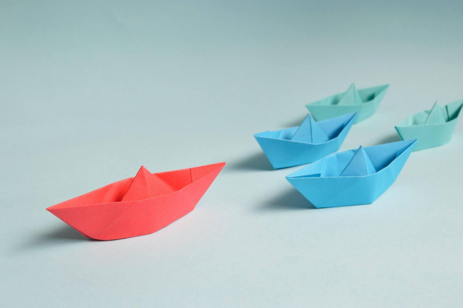 Rood papieren bootje dat afwijkt van blauwe bootjes als symbool voor eigen koers, identiteit en mentale weerbaarheid