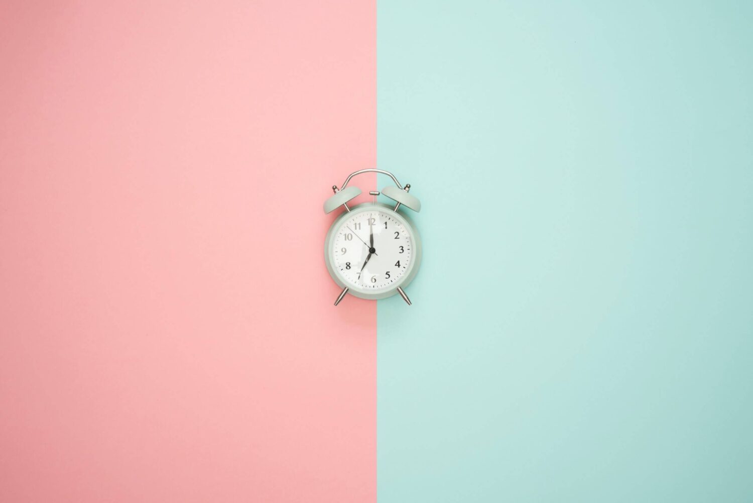 Wekker tegen een achtergrond die half roze en half lichtblauw is