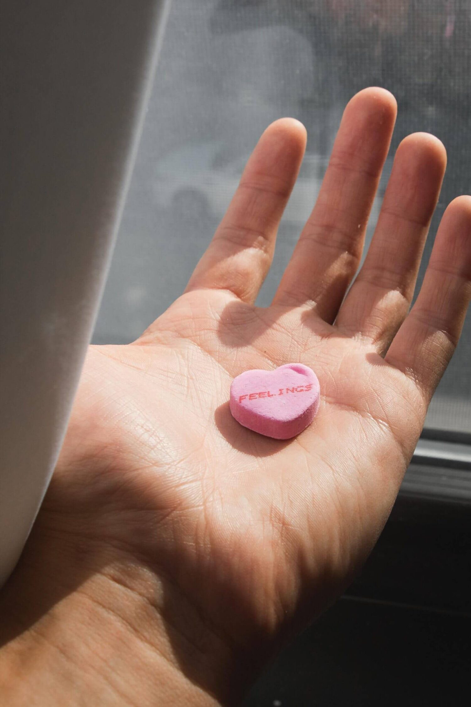 Hand met een roze hartvormig snoepje waarop “feelings” staat