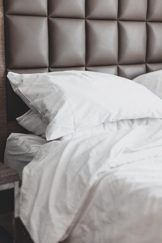 Opgemaakt bed met witte kussens en dekbed tegen een gestoffeerd hoofdbord