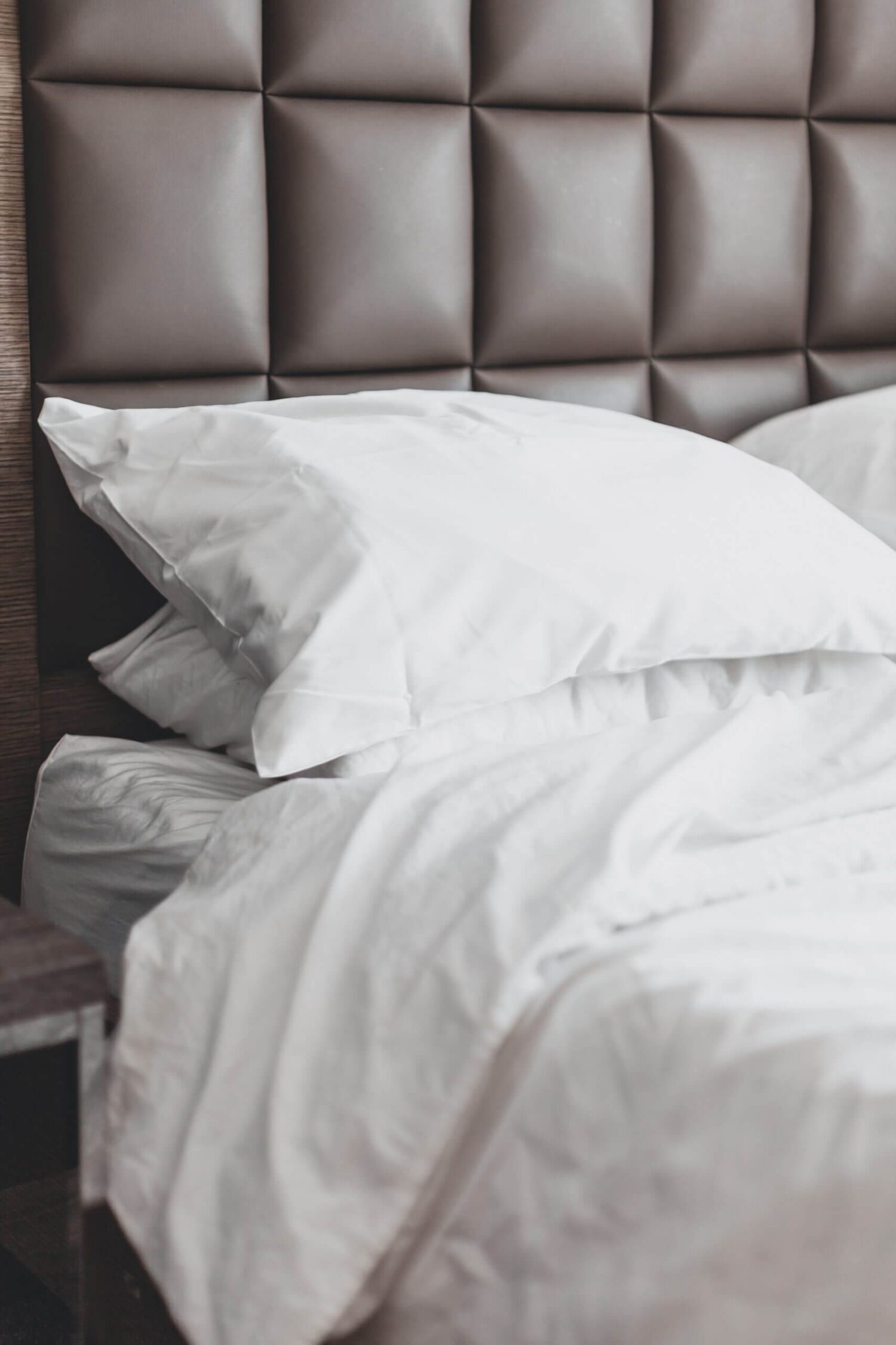 Opgemaakt bed met witte kussens en dekbed tegen een gestoffeerd hoofdbord