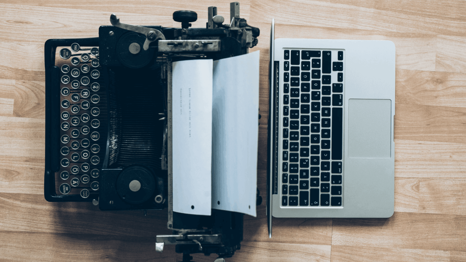 Oude typemachine naast een moderne laptop op een houten tafel