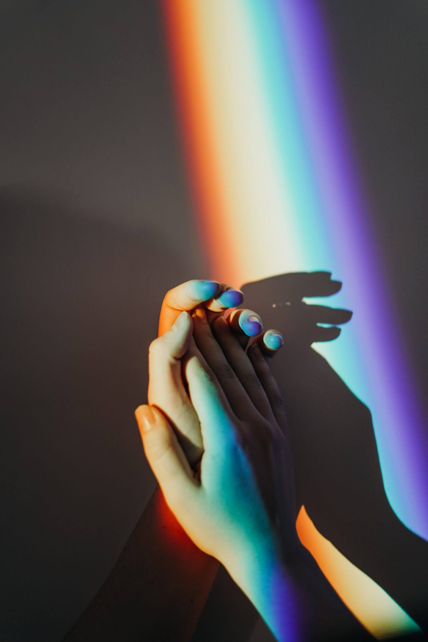 Handen in gekleurd licht van een regenboog die op een muur schijnt