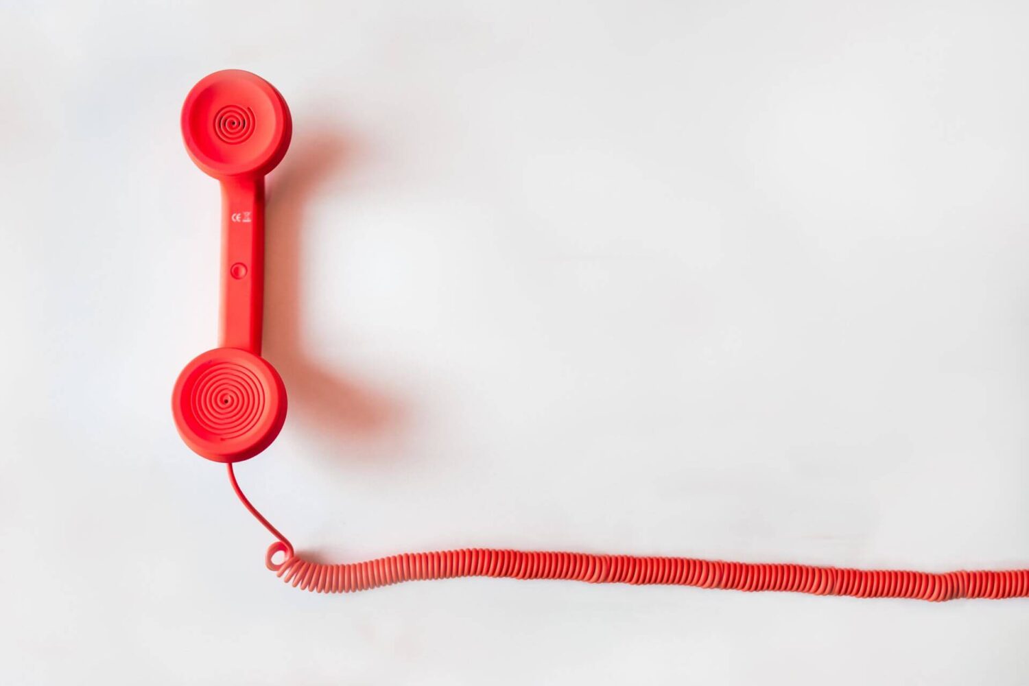 Rode telefoonhoorn met snoer tegen een lichte achtergrond