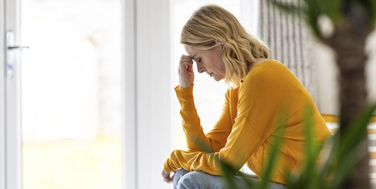 Vrouw zit voorovergebogen met haar hand tegen haar hoofd en kijkt somber