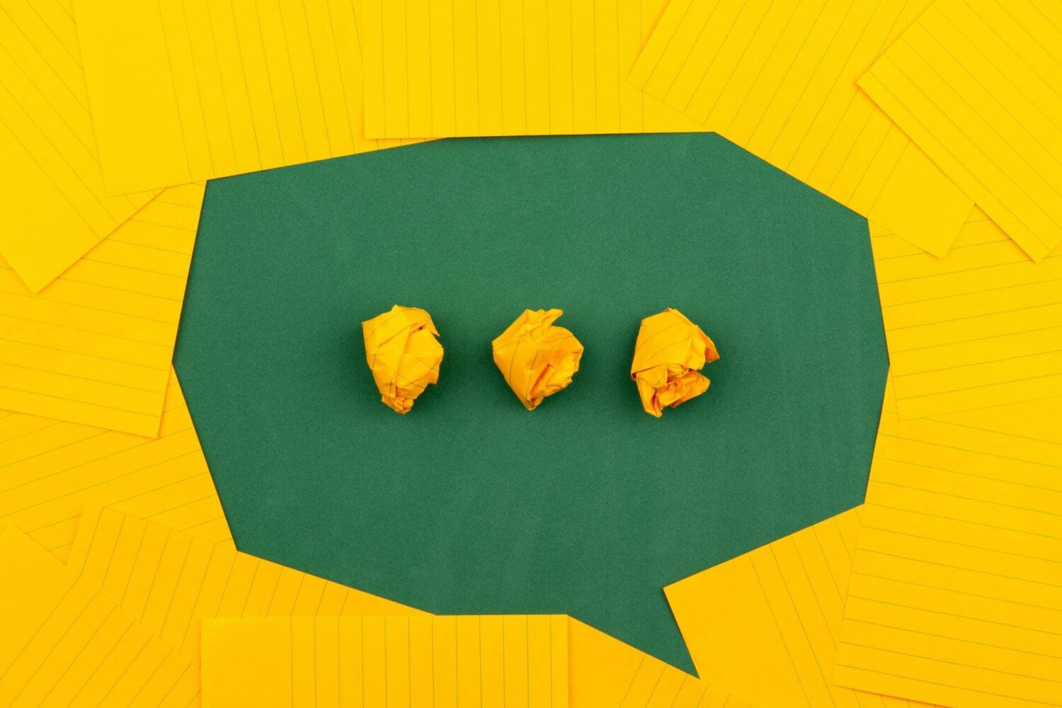 Drie verfrommelde papieren propjes in een tekstballon op een gele achtergrond