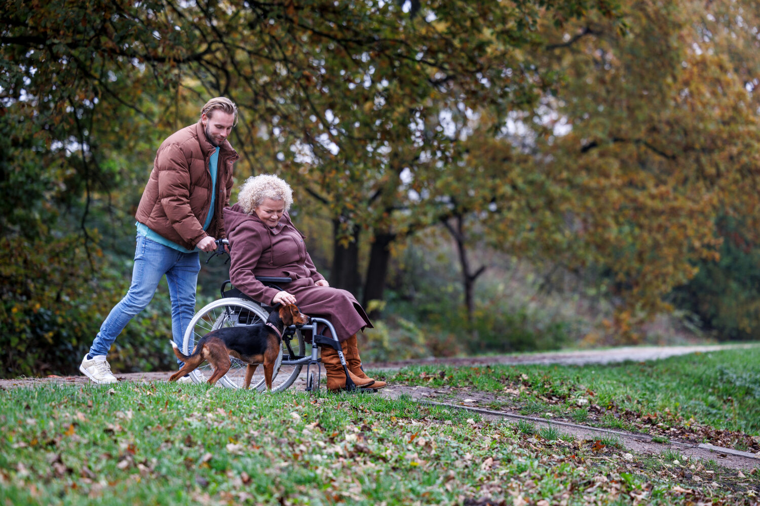 Man helpt vrouw in rolstoel tijdens wandeling in park, symbool voor zorg, ondersteuning en welzijn