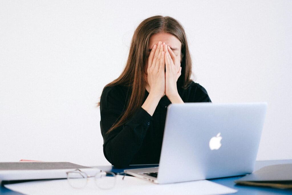 Vrouw zit achter laptop en houdt handen voor gezicht van stress