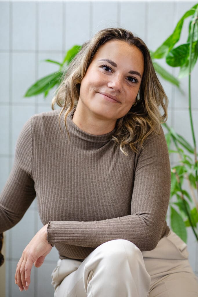 Vrouw met bruine trui en vriendelijke uitstraling kijkt in camera