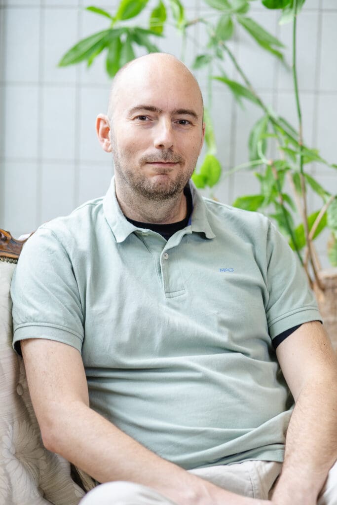 Man met groen shirt en rustige uitstraling zit op stoel en kijkt in camera