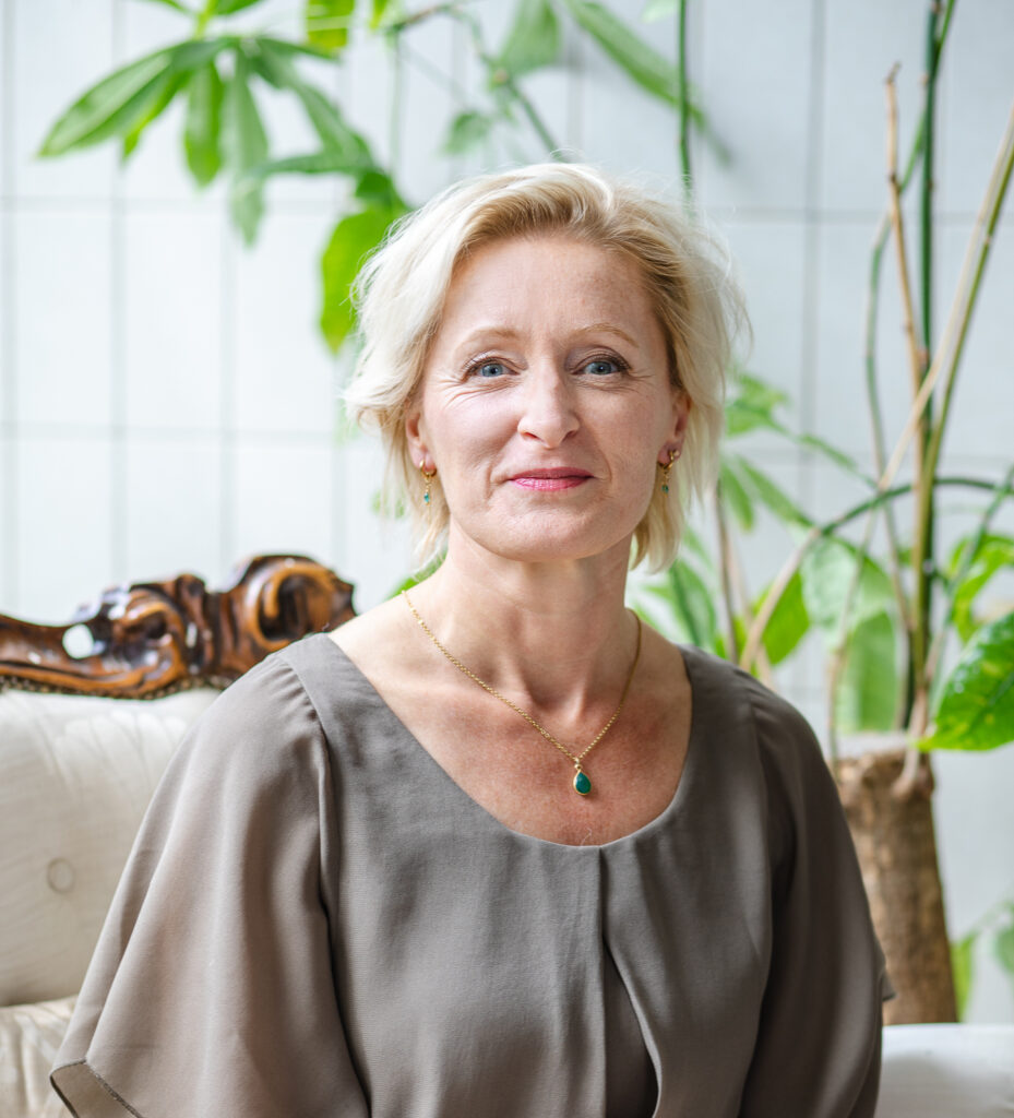 Vrouw met korte blonde haren en vriendelijke uitstraling kijkt in camera