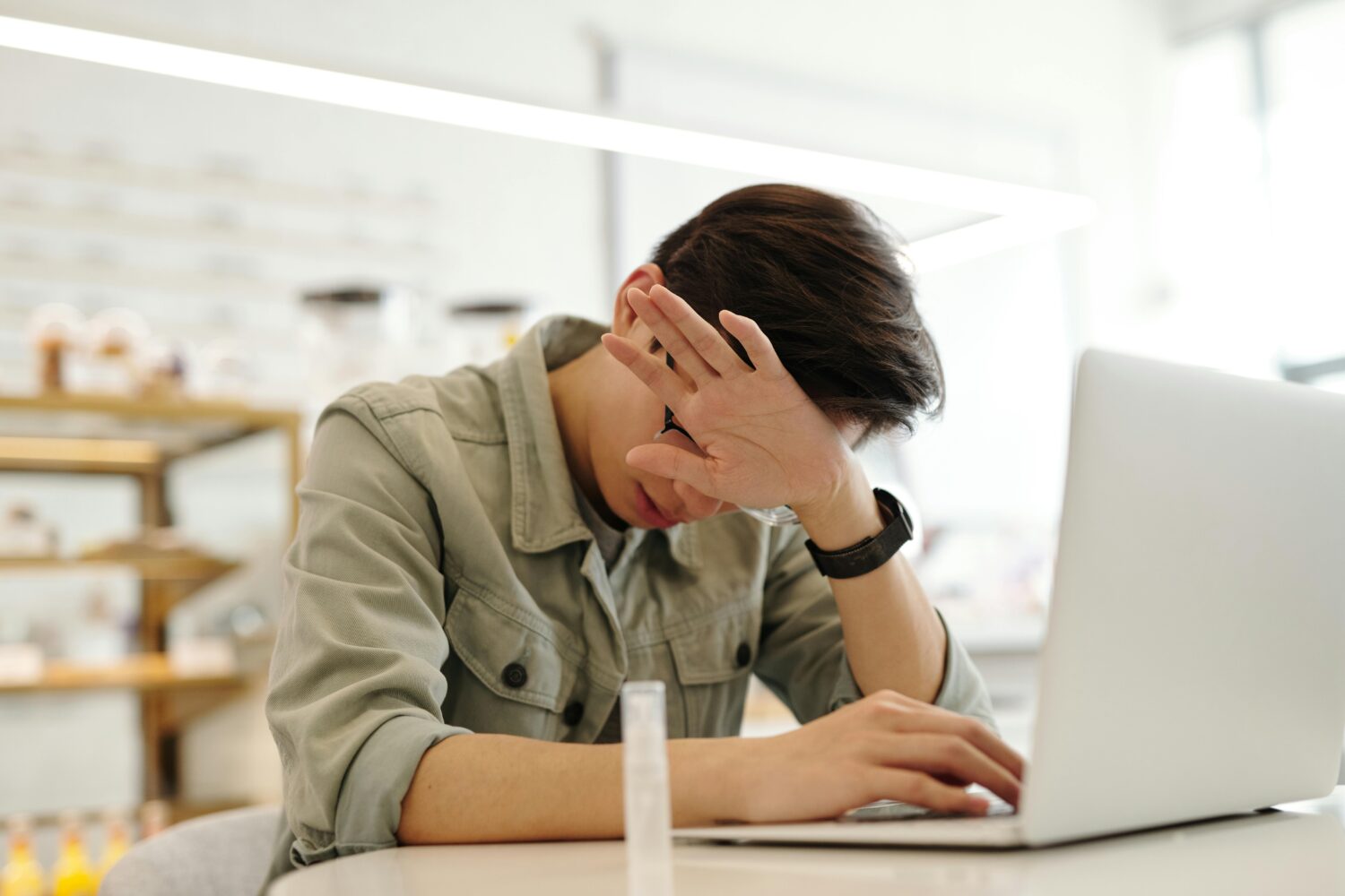 Jongen zit vermoeid achter laptop en houdt hand voor gezicht