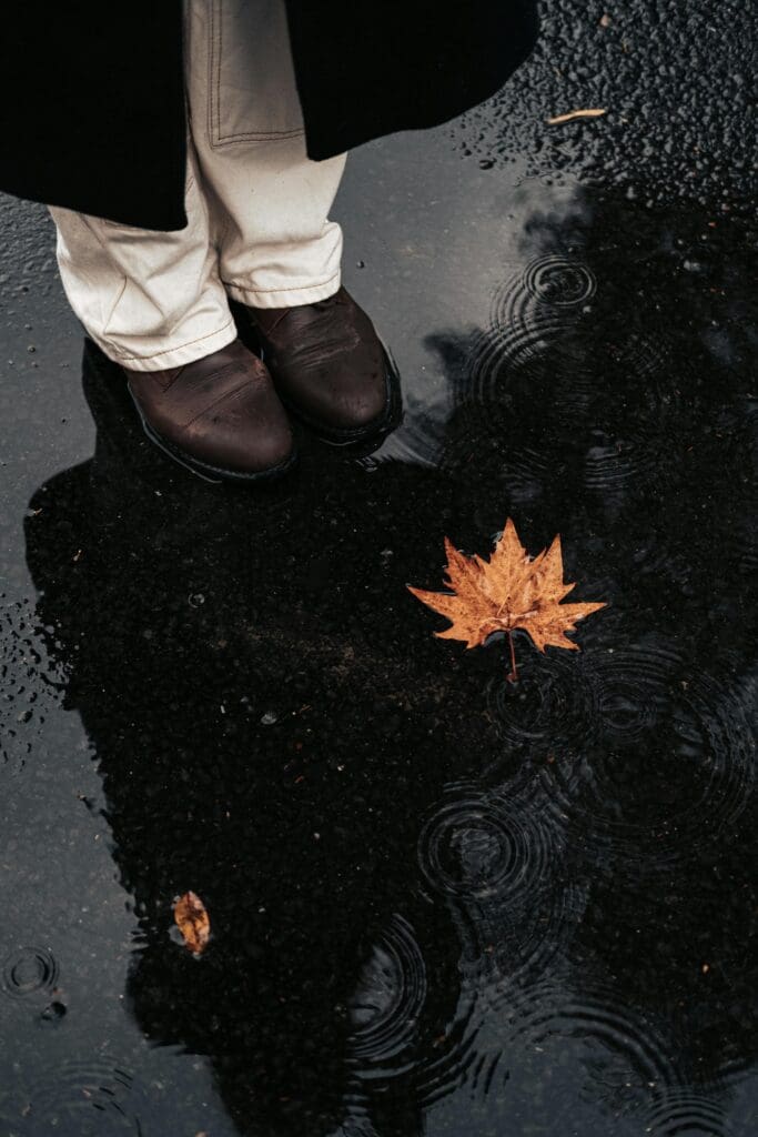 Persoon staat bij plas water met reflectie en herfstblad op natte grond