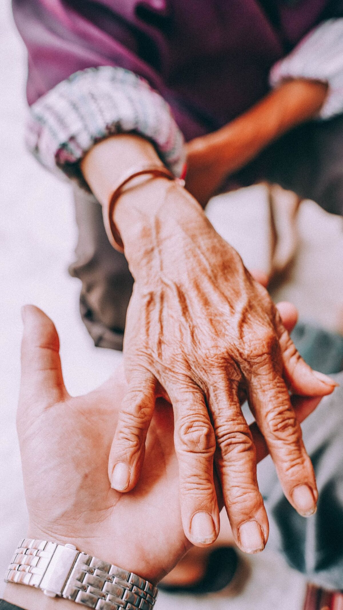 Een oudere hand rust op de open hand van een jongere persoon als teken van zorg, ondersteuning en vertrouwen. Beide handen staan centraal in beeld, met een onscherpe achtergrond.