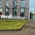 Grote witte VerdiGroep-belettering op een gazon voor een modern kantoorgebouw met grijsbruine bakstenen, hoge ramen en een glazen entree.