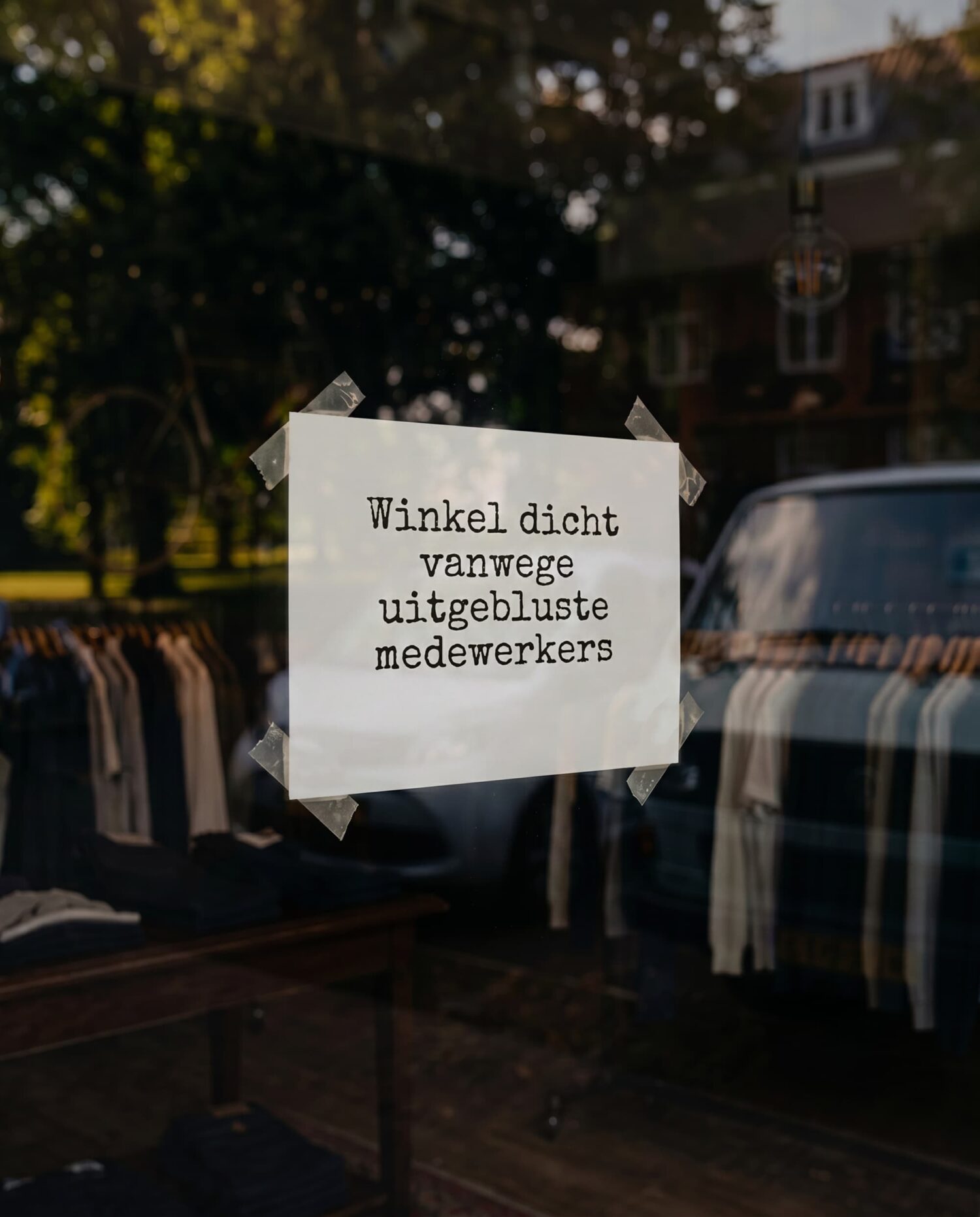 Briefje op de etalageruit van een kledingwinkel met de tekst 'Winkel dicht vanwege uitgebluste medewerkers